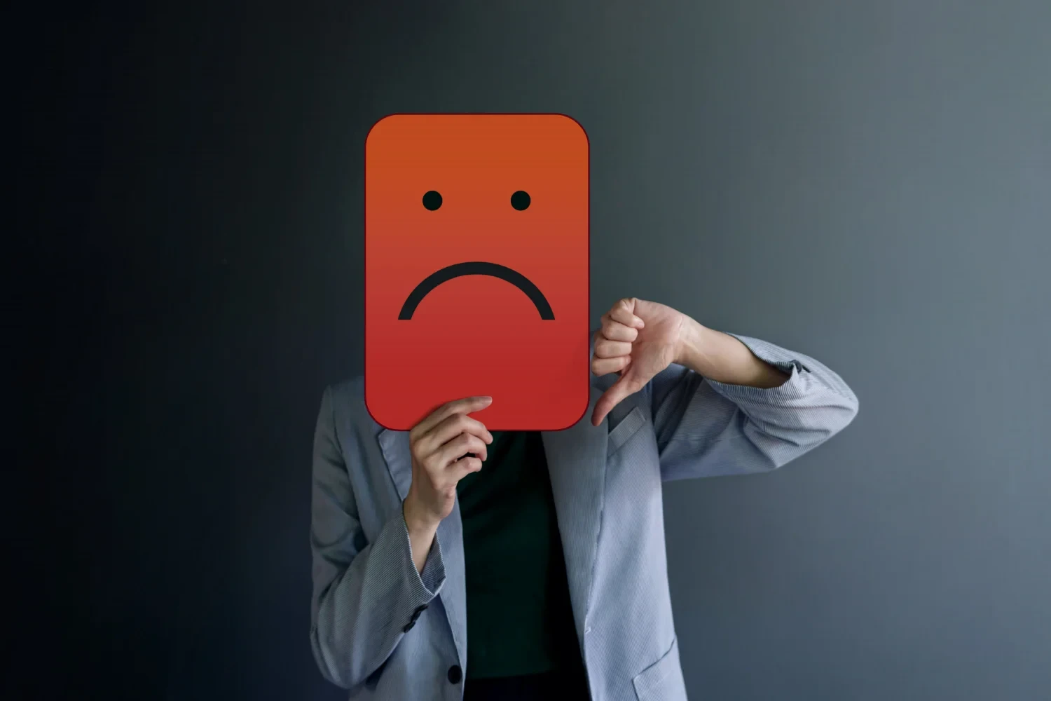 Pessoa segurando uma placa em frente ao rosto com desenho de uma expressão que sugere um cliente insatisfeito.