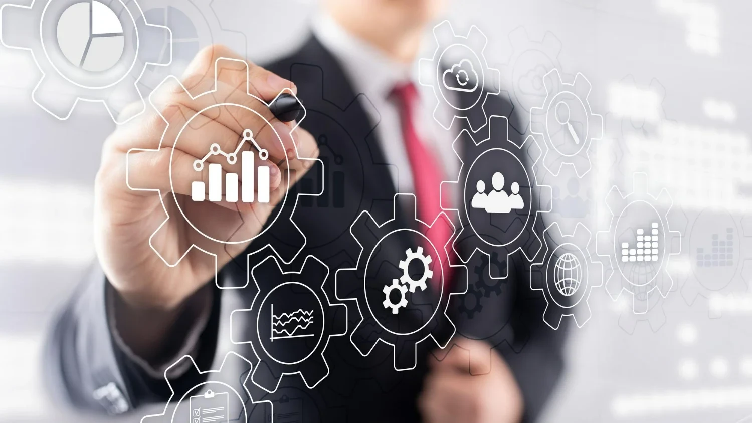 Homem branco de terno com caneta na mão apontando para imagens gráficas de engrenagens que representam softwares de gestão.