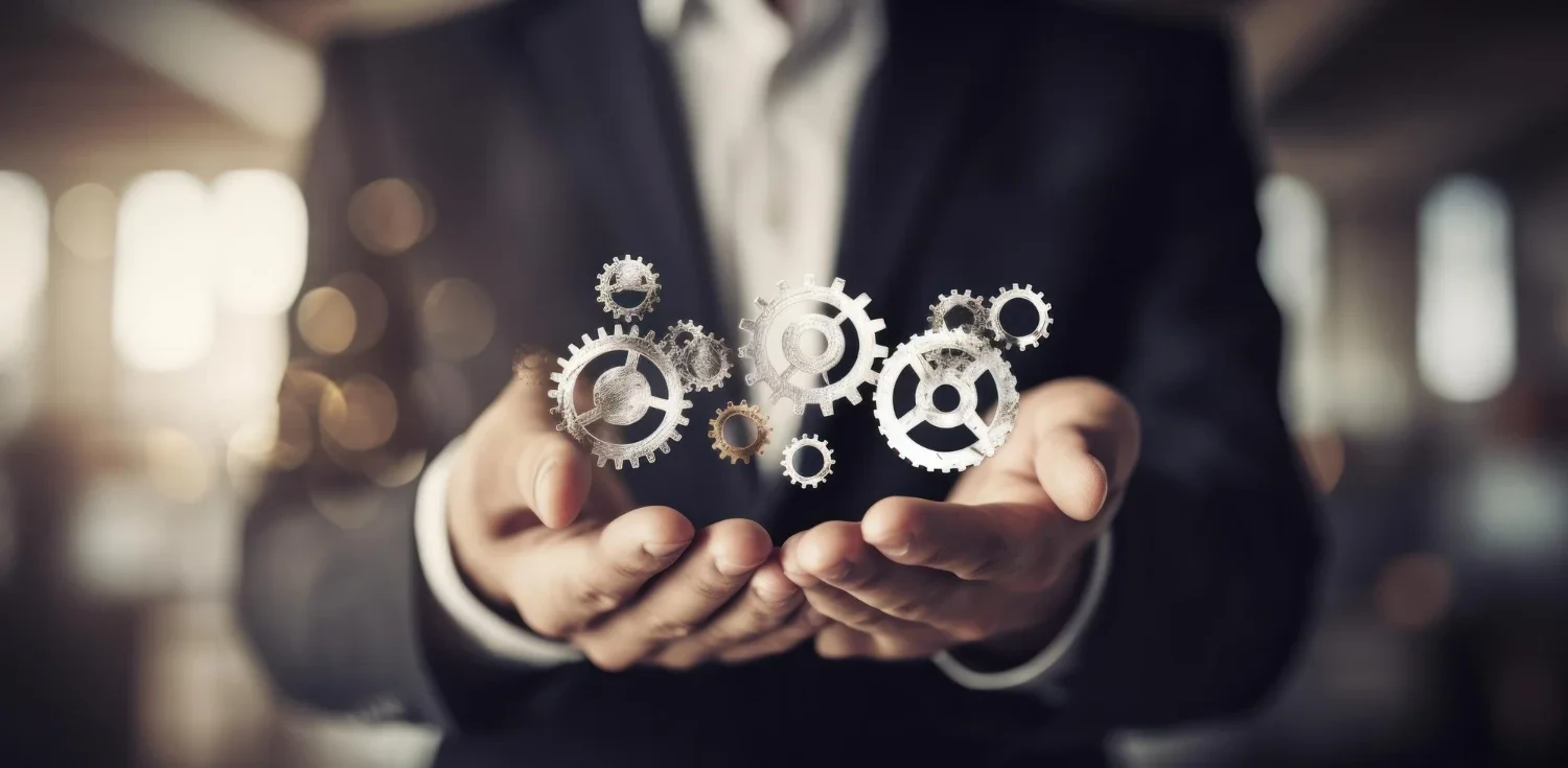 Pequenas engrenagens sobre as mãos unidas de um homem branco de terno representando o funcionamento da empresa com as técnicas de autogerenciamento.