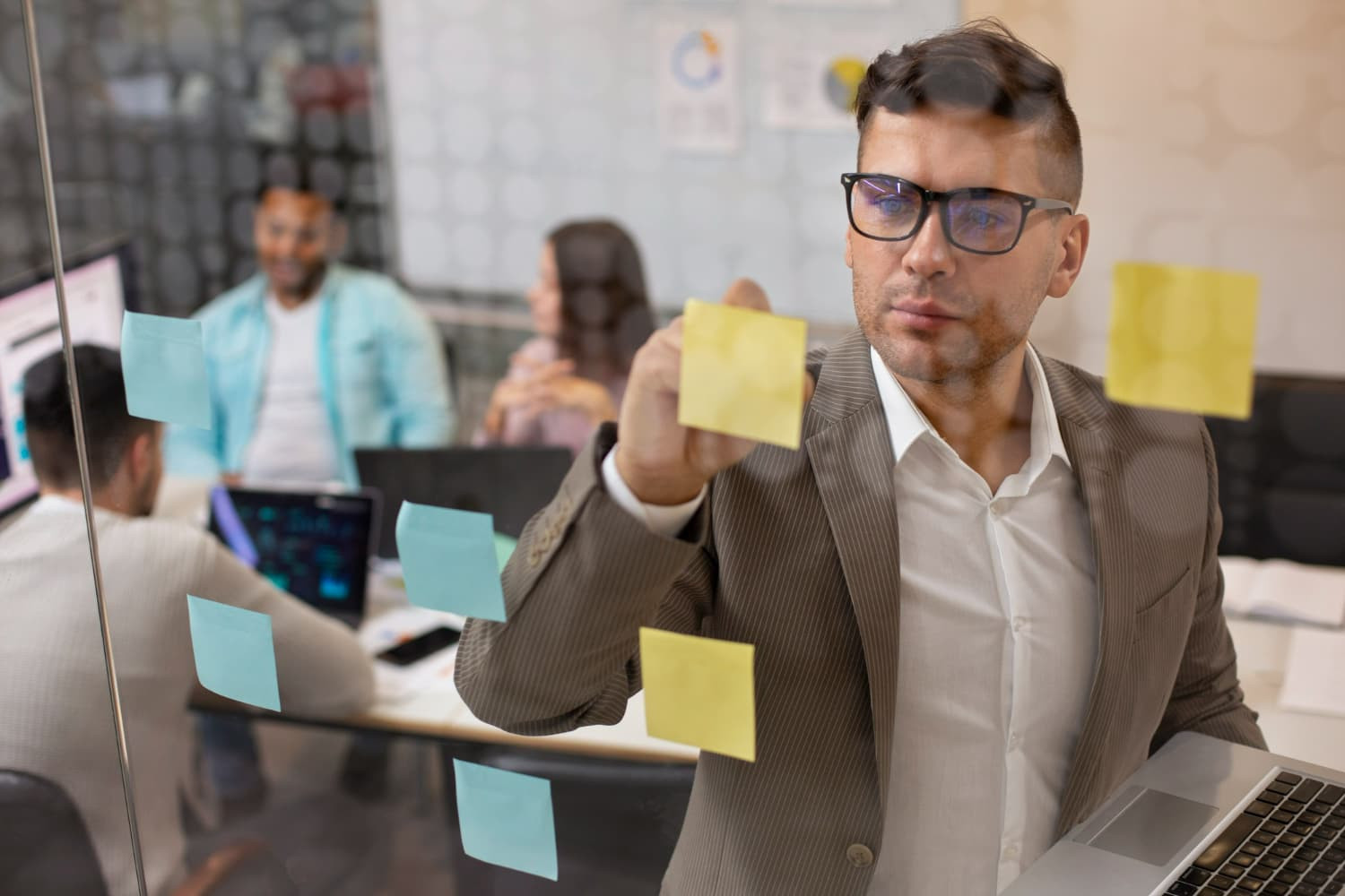 Homem branco de terno claro fazendo anotações em post-its colados em um vidro, exercitando o autogerenciamento no trabalho.